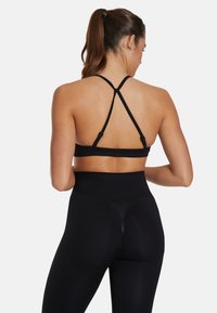 Zwarte sportbh met racerbackontwerp, verstelbare bandjes en naadloze constructie, gecombineerd met hoge taille zwarte leggings.