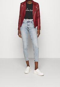 Röd läder bikerjacka, svart grafisk t-shirt, ljusblå slim fit-jeans, vita sneakers; funktioner inkluderar dragkedjor, figursydd design och uppvikta ärmar.