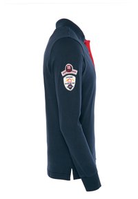 Jūros tamsiai mėlynos spalvos polo marškiniai su raudonu apykakle. Yra išsiuvinėtas logotipas kairiajame rankove ir šonuose yra plyšiai. 