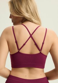 Bordowa, bezszwowa bielizna braletowa o strukturze żebrowej, z regulowanymi krzyżującymi się ramiączkami i elastycznym dołem. Dopasowany krój.