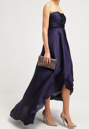 Robe bleu marine bustier haute en bas avec un corsage plissé, tissu fluide, portée avec des escarpins neutres et une pochette métallique.