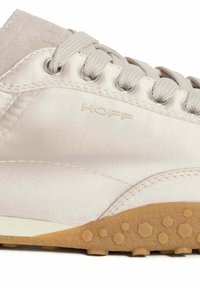 Zapatilla de color beige claro con material satinado, que presenta una suela de goma con patrones hexagonales y ojales en tono plateado para los cordones. Logo "HOFF" en el lateral.