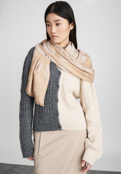 Strikket cardigan i grått og kremfarge med kabelmønstre, knappefront. Drapert beige skjerf med subtile mønstre, kombinert med en beige nederdel.