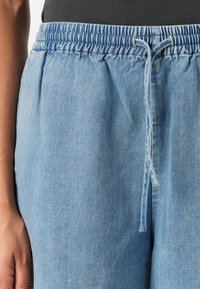Svijetloplavi traper hlače-jogger s elastičnim pojasom, zatvaranjem na vezicu i ležernim krojem. Mekana tekstura bez vidljivih uzoraka.