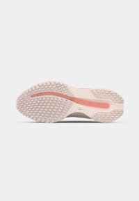 Semelle d'une chaussure de sport beige et orange avec un motif de grip texturé et un logo Nike visible au centre.