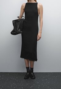 Robe noire sans manches avec une silhouette droite, accompagnée d'un sac tote noir texturé et de mocassins noirs avec des détails texturés.