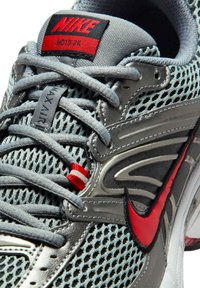 La zapatilla Nike Moto 2K presenta una parte superior de malla gris con acentos plateados, logo rojo y cordones texturizados para un ajuste seguro. La suela de goma mejora el agarre.