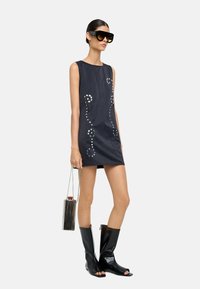 Czarna, bezrękawnikowa mini sukienka z srebrnymi zdobieniami, w połączeniu z czarnymi butami na odkrytych palcach oraz dużymi okularami przeciwsłonecznymi. W zestawie torebka z metalicznymi frędzlami.