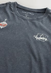 Tricou din bumbac de culoare albastru închis, cu un grafic de ornament de Crăciun și textul "MERRY XMAS" însoțit de cărți de joc. Design clasic cu guler rotund.