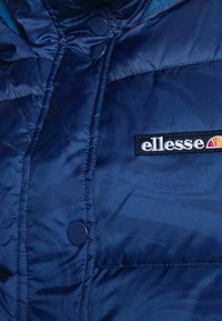 Granatowa kurtka puchowa o błyszczącej fakturze, z wysokim kołnierzem, zatrzaskami oraz naszywką z logo Ellessee z przodu.