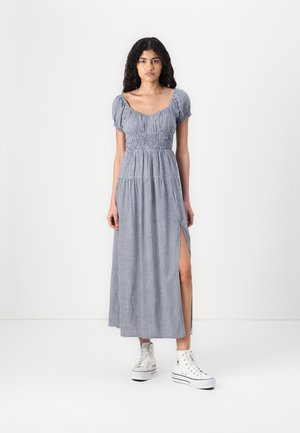 Blue and white checkered maxi dress with short puff sleeves, smocked bodice, and side slit, paired with white high-top sneakers.