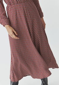 Pitkä punainen hame, jossa on geometrinen valkoisen ja sinisen kuvio. Pehmeä, valuva kangas, keskikorkea malli ja mukava istuvuus.