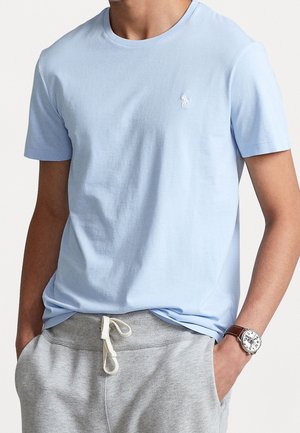 Jasnoniebieska bawełniana koszulka z okrągłym dekoltem i krótkimi rękawami, z małym białym logo na piersi, w połączeniu z szarymi spodniami dresowymi.