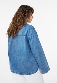 Lyseblå denimjakke med afslappet pasform, lange ærmer, spidst krave og synlige syningsdetaljer.