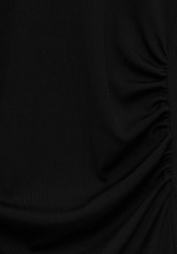 Gros plan sur un tissu noir avec un détail élastique froncé créant des plis texturés sur le côté droit.