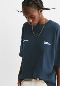 Marineblå oversized t-shirt lavet af blødt stof. Har hvid broderet tekst "Dare More" og "Make Memories" på forsiden.