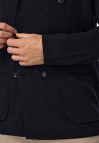 Must mustriga kardigan tekstuuriga viimistlusega, millel on kaks esist pocketit ja mustad nööbid. Disain sisaldab vabalt langevat kraed ja peeneid varrukaid.