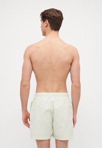 Shorts de bain vert clair avec une texture lisse et légère, taille élastique et une poche arrière unique. Le modèle est présenté de dos.