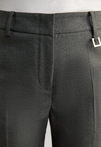 Graue maßgeschneiderte Hosen mit glatter Textur, gerade geschnitten, mit Gürtelschlaufen und einem Metallverschluss. Subtiles Stoffmuster sichtbar.