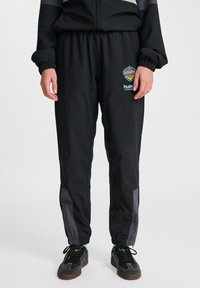 Svarta träningsbyxor med elastisk midja och muddar. Har grå sidopaneler och logotyper på vänster lår. Tillverkade av ett mjukt, lätt material.