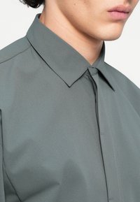 Γκρίζο πουκάμισο με κουμπιά και υφή, με κλασικό γιακά και κρυφά κουμπιά. Το ύφασμα φαίνεται απαλό και λείο.