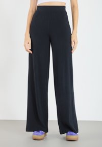 Vida byxor i ribbat tyg, med hög midja i en mörk marinblå färg. Tyget har en slät textur med vertikala linjer.