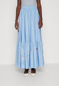 Ljusblå maxi kjol i bomull med broderade blommönster, veckad midja och volangkant. Bärs med vita klackskor.