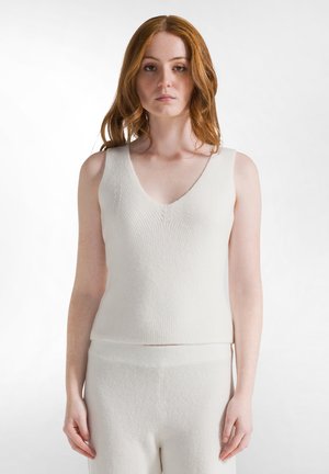 Top sin mangas de punto blanco con cuello en V, que presenta una silueta ajustada y una textura suave, combinado con pantalones blancos a juego.