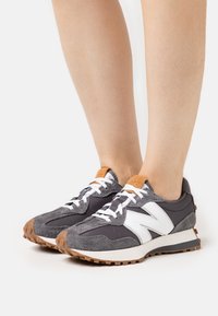 Grå och vita sportiga sneakers med en blandning av mocka och tyg, med en gummisula och kontrasterande bruna detaljer på hälen.