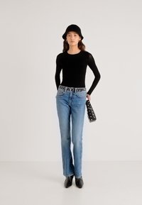 Zwarte top met lange mouwen, lichtblauwe jeans met rechte pijpen, zwarte riem met ronde accenten, en een zwarte handtas met studs. Zwarte enkellaarsjes.