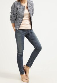 Granatowa bomberka z delikatnym wzorem na beżowej bluzce, zestawiona z ciemnoniebieskimi obcisłymi jeansami i cielistymi balerinami w wzór węża.