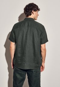 Mörkgrön kortärmad skjorta i en texturerad, linne-liknande tyg; har en klassisk krage och detaljer i ryggen.