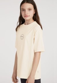 T-shirt en coton couleur crème à manches courtes, arborant un logo graphique noir sur la poitrine, coupe loose avec un col rond.