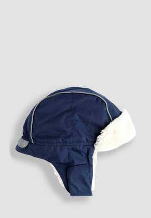 Mørkeblå vintertrapperhat med hvid faux pelsforing og øreringe på en neutral baggrund.