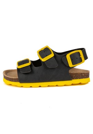 Sandale noire avec des accents jaunes et des boucles. Dotée d'une semelle en liège et d'une semelle en caoutchouc jaune durable. Le design comprend des sangles réglables.