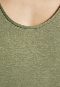 Gros plan sur l'encolure d'un t-shirt vert clair à col rond montrant la texture du tissu et la peau au-dessus du col.