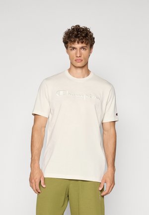T-shirt en coton crème avec un col rond, des manches courtes et le logo "Champion" brodé. Associé à un pantalon vert olive.