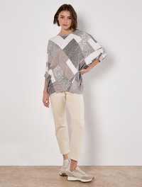 Graues und weißes geometrisches Muster-Oversized-Oberteil mit drei Viertelärmeln, kombiniert mit cremefarbenen Slim-Fit-Hosen und hellgrauen Turnschuhen.