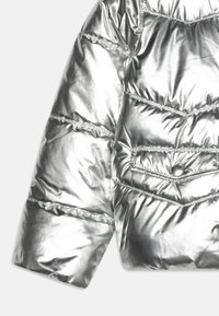 Ασημί μεταλλικό μπουφάν puffer με κεντημένες περιοχές, τσέπη με κουμπί και γυαλιστερή υφή; ελαφρύ με cropped σχέδιο.
