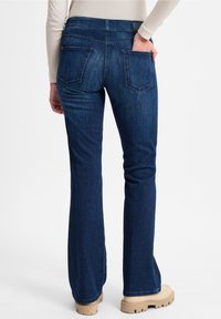 Vaqueros acampanados azul oscuro con una cintura de altura media, bolsillos traseros visibles y una textura de denim suave. Se combinan con calzado de colores claros.