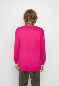 Rosa sweatshirt med långa ärmar, rund halsringning och elastiska muddars. Mjuk textur, avslappnad passform, bärs med olivgröna kordbyxor.