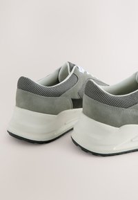 Par grå og hvide løbesko med mesh og ruskindoverdel, tykke hvide såler og hvide snørebånd på en neutral baggrund.
