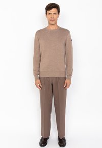 Brązowy sweter z dzianiny o okrągłym dekolcie, zestawiony z jasnobrązowymi spodniami i ciemnymi butami. Sweter ma prążkowaną fakturę oraz detale na ramionach.