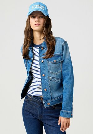 Jeansjacka i ljusblått med knappstängning och två bröstfickor, ihop med en randig topp i marinblått och vitt samt mörkblå jeans. Kapsyl med texten "En legend i jeans."