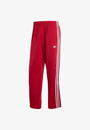 Pantalones deportivos Adidas rojos con cintura elástica, franjas laterales blancas y logo Trefoil en el muslo derecho sobre fondo blanco.