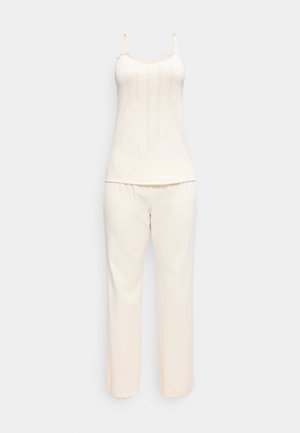 Kremfarvet ribstrikket pyjamassæt med top med spaghettistropper og bukser med lige ben med subtile lyserøde prikker.