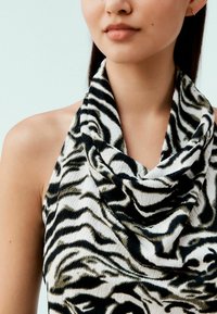 Haut à col bénitier en tissu doux avec un motif rayé zèbre noir et blanc et une texture subtile. Gros plan sur le décolleté et l'épaule supérieure.