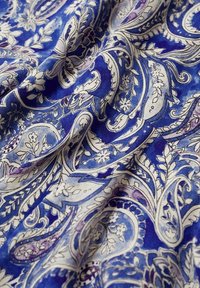 Tessuto blu con motivo paisley e accenti floreali bianchi e viola, texture morbida e design fluido.