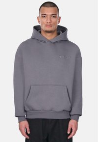 Grijze hoodie met een kangoeroezak, ribbelmanchetten en een klein geborduurd logo op de borst. Gemaakt van zachte, textuurstof.