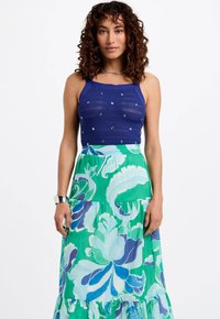 Top lavorato a maglia blu navy con decorazioni, abbinato a una gonna maxi floreale verde con disegni blu e teal e orlo a balze.